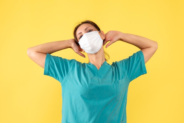 Front view female doctor in medical shirt and mask on yellow background