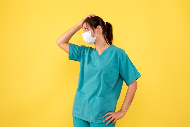 Front view female doctor in medical shirt and mask on yellow background