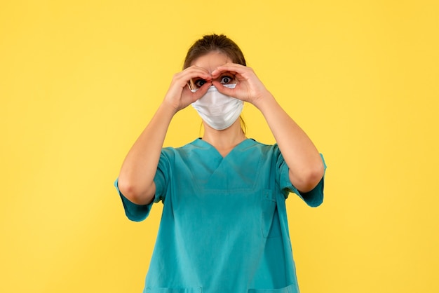 Front view female doctor in medical shirt and mask on yellow background