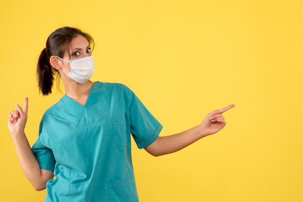 Front view female doctor in medical shirt and mask on yellow background