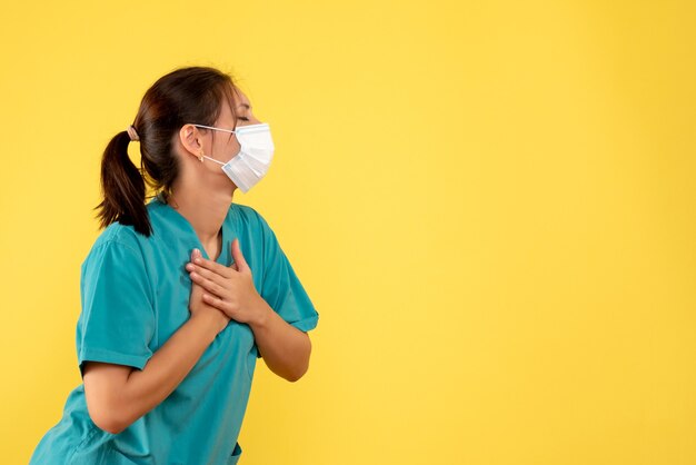 Front view female doctor in medical shirt and mask on yellow background