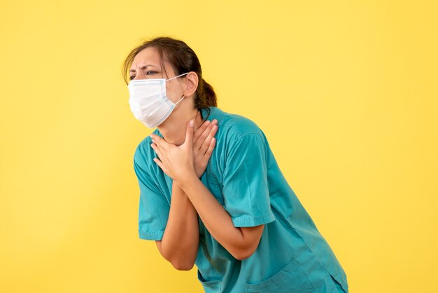 Front view female doctor in medical shirt and mask on yellow background