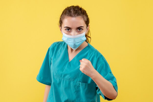 Medico femminile di vista frontale in camicia medica e maschera sulla pandemia covid di colore di salute del virus dell'uniforme da scrivania gialla