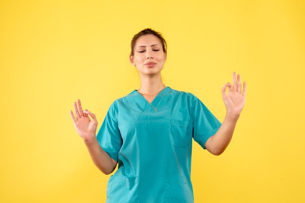 Front view female doctor in medical shirt meditating on yellow background