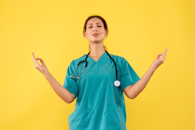 黄色の背景で瞑想する医療シャツの正面図の女性医師