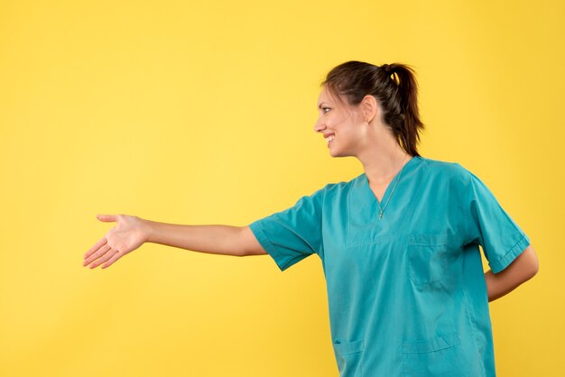 黄色の背景に手を振る医療シャツの正面図女性医師