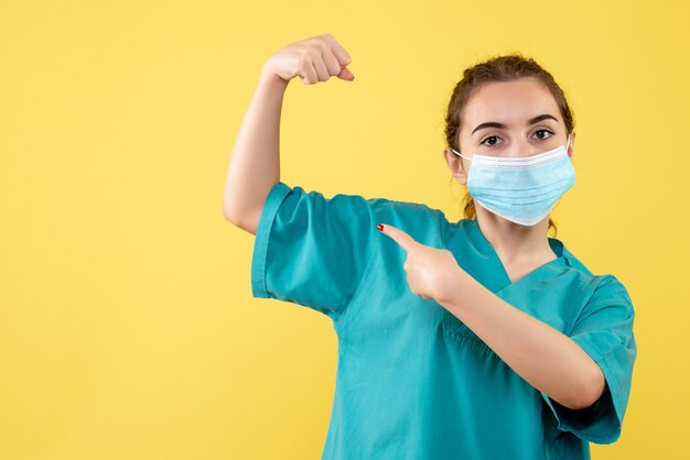 Front view female doctor in medical shirt and sterile mask flexing, health virus uniform color covid-19 emotion