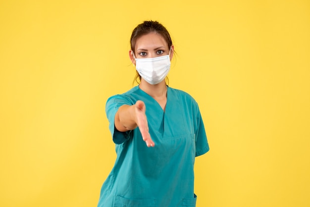 의료 셔츠와 노란색 배경에 멸균 마스크 인사말에 전면보기 여성 의사