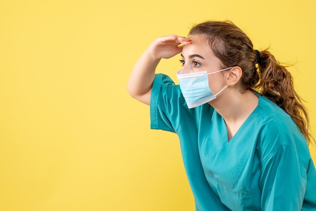 医療シャツと滅菌マスクを身に着けた正面図の女性医師が距離を見て、健康ウイルスの均一な色を提供します-
