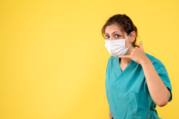 Front view female doctor in medical shirt and sterile mask on a yellow background