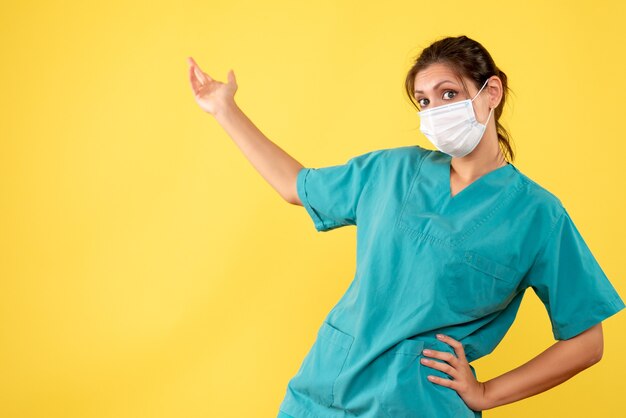 Front view female doctor in medical shirt and sterile mask on the yellow background