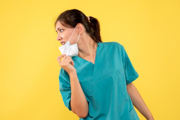 Front view female doctor in medical shirt and sterile mask on yellow background