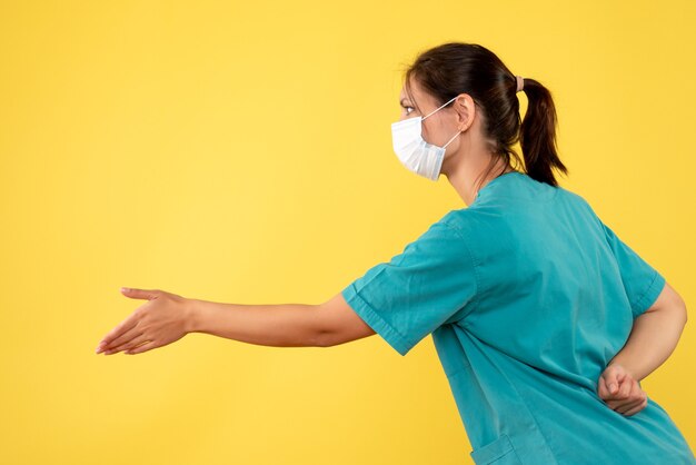 黄色の背景に医療シャツと滅菌マスクの正面図の女性医師