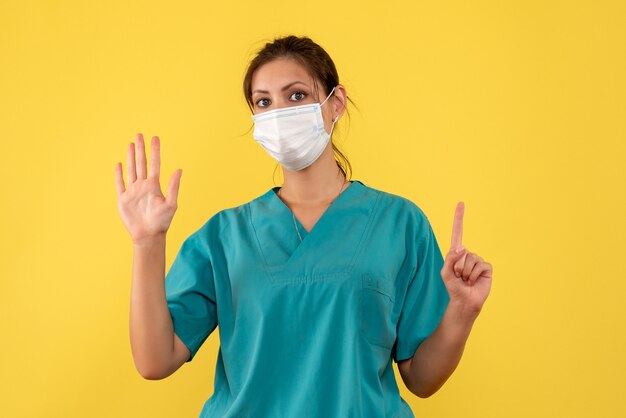 Front view female doctor in medical shirt and sterile mask on yellow background