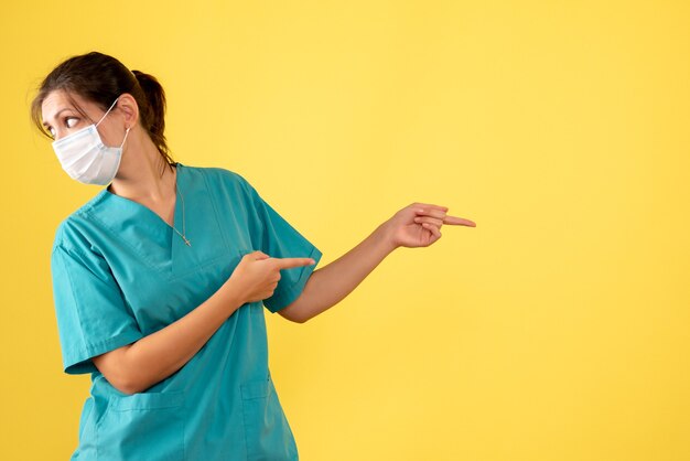 의료 셔츠와 노란색 배경에 멸균 마스크 전면보기 여성 의사
