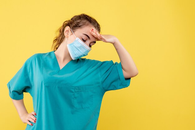 医療シャツと黄色い机の上の滅菌マスクの正面図女性医師パンデミックカラー健康制服covid-19ウイルス