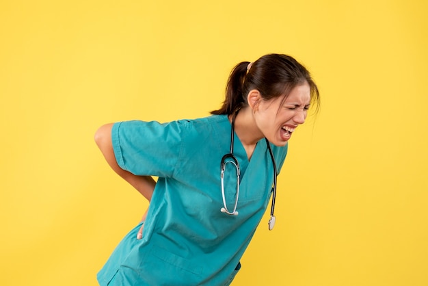 Front view female doctor in medical shirt suffering from back ache on yellow background