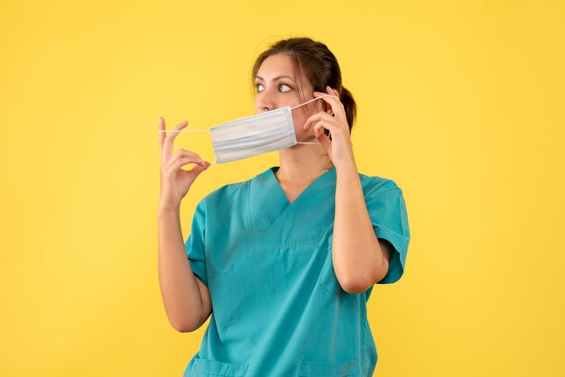 Front view female doctor in medical shirt taking off her mask on yellow background