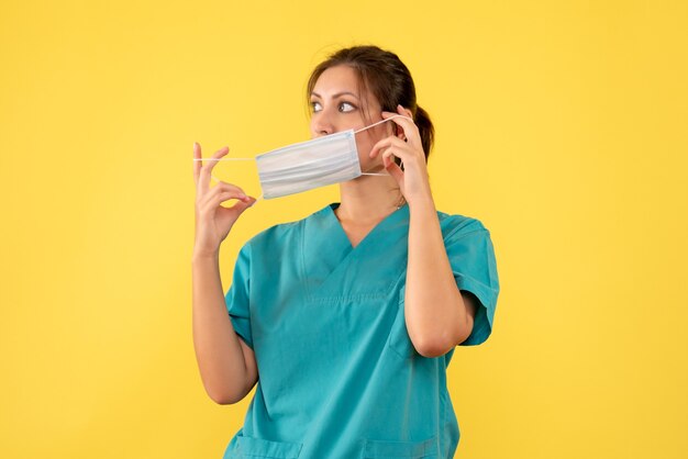 Вид спереди женщина-врач в медицинской рубашке, снимая маску на желтом фоне