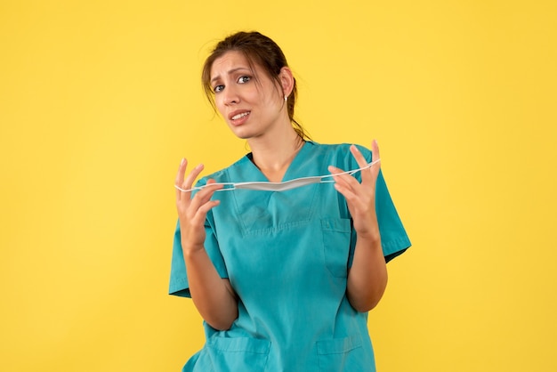Foto gratuita medico femminile di vista frontale in camicia medica che toglie la maschera sterile su fondo giallo