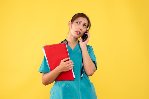 黄色の背景で電話で話している医療シャツの正面図の女性医師