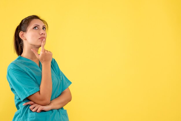 Front view female doctor in medical shirt thinking on a yellow background