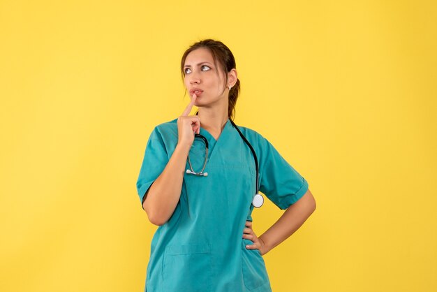 Front view female doctor in medical shirt thinking on yellow background