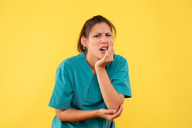 Front view female doctor in medical shirt with pain in her arm and tooth on yellow background