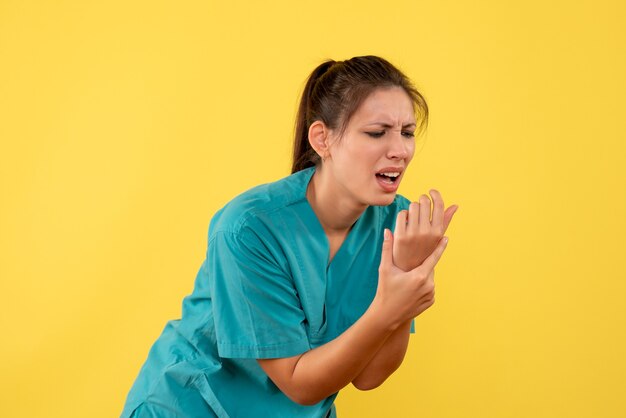 Front view female doctor in medical shirt with pain in her arm on the yellow background