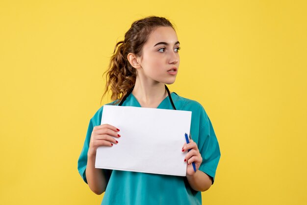 Front view of female doctor in medical shirt with papers and stethoscope on yellow wall