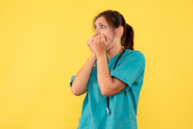 Front view female doctor in medical shirt with scared face on yellow background