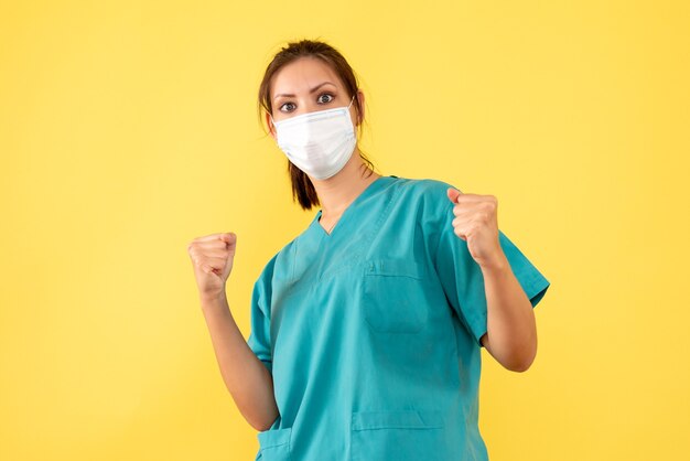 黄色の背景に喜んで滅菌マスクと医療シャツの正面図の女性医師