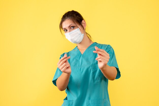 Front view female doctor in medical shirt with sterile mask on the yellow background