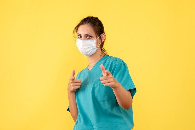 의료 셔츠와 노란색 배경에 멸균 마스크 전면보기 여성 의사