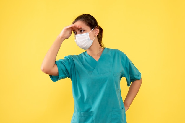 Medico femminile vista frontale in camicia medica e con maschera sterile su sfondo giallo