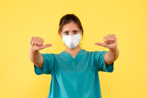 Вид спереди женщина-врач в медицинской рубашке и стерильной маске на желтом фоне