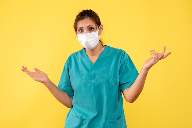 Вид спереди женщина-врач в медицинской рубашке и стерильной маске на желтом фоне