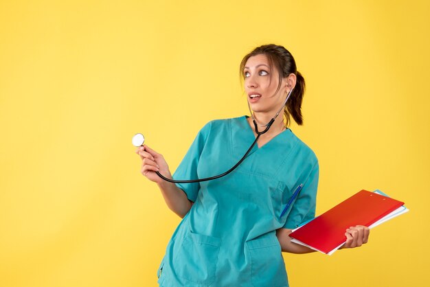 노란색 배경에 청진 기 및 메모와 함께 의료 셔츠에 전면보기 여성 의사
