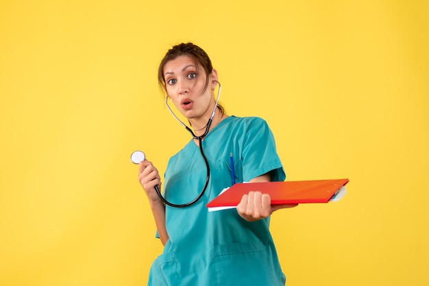 Front view female doctor in medical shirt with stethoscope and notes on yellow desk hospital medic emotion covid- health virus color