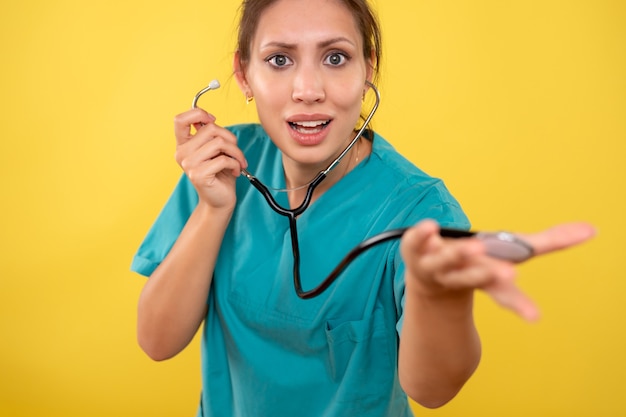 Вид спереди женщина-врач в медицинской рубашке со стетоскопом на желтом фоне