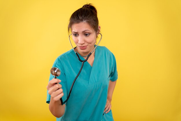 Front view female doctor in medical shirt with stethoscope on yellow background