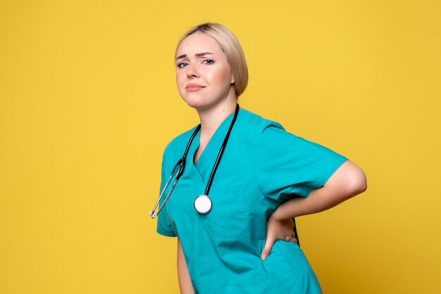Front view of female doctor in medical shirt with stethoscope on a yellow wall