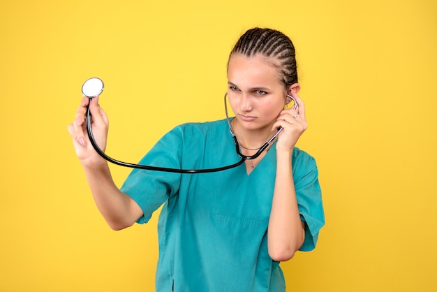 Front view of female doctor in medical shirt with stethoscope on a yellow wall