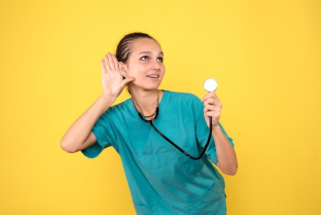 Front view of female doctor in medical shirt with stethoscope on the yellow wall