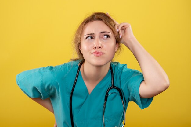 Front view of female doctor in medical shirt with stethoscope on yellow wall