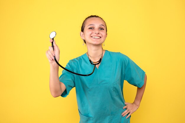 Front view of female doctor in medical shirt with stethoscope on yellow wall