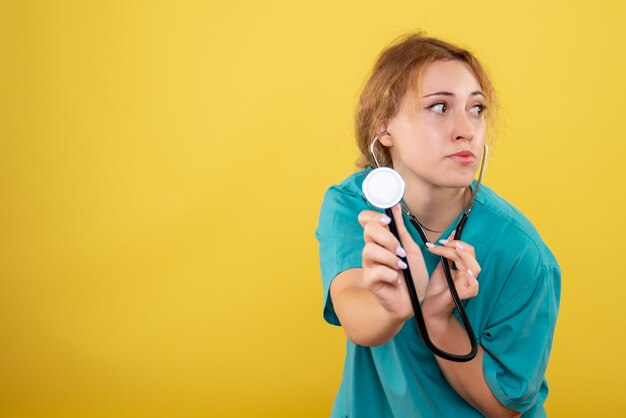 Front view of female doctor in medical shirt with stethoscope on yellow wall