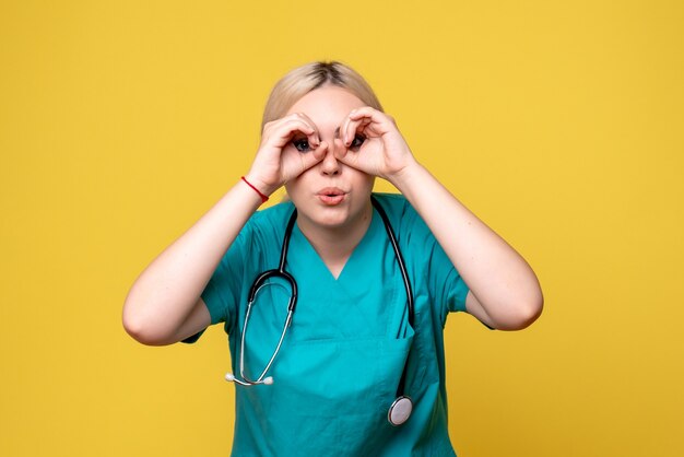 Front view of female doctor in medical shirt with stethoscope on yellow wall