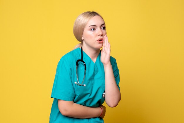 黄色の壁に聴診器と医療シャツの女性医師の正面図