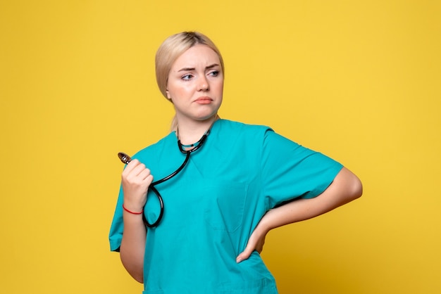 Front view of female doctor in medical shirt with stethoscope on yellow wall